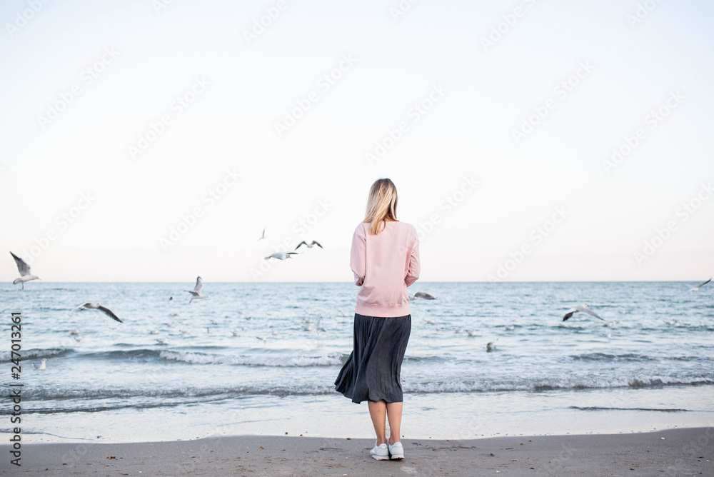 A girl stands on the beach and seagulls are flying nearby. Enjoy the moment. Rest and relaxation by the sea. Weekend in nature. Life style A girl stands on the beach and seagulls are flying nearby. Enjoy the moment. Rest and relaxation by the sea. Weekend in nature. Life style