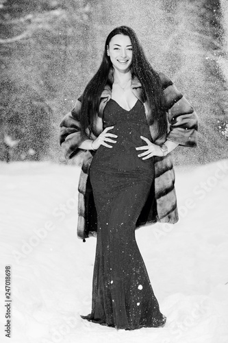 Yang beautiful woman poses a snow-covered winter forest in long red dress.