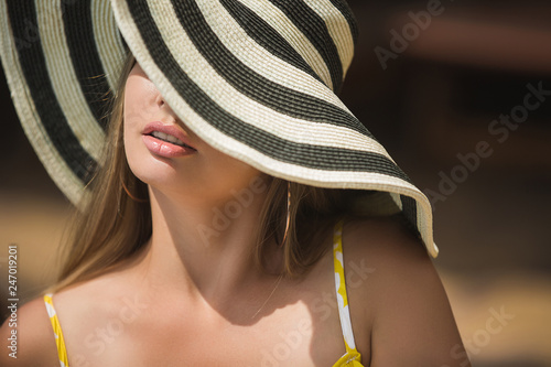 Young woman summer portrait closeup. Lady in the hat. Female leisure. Girl covering her face with stripped hat photo