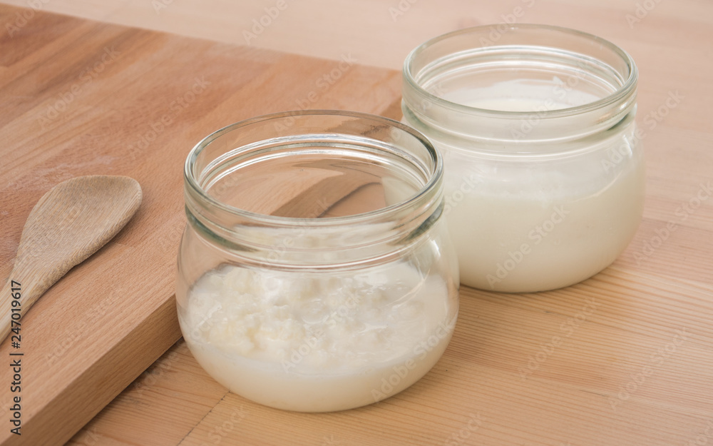 Organic Kefir and kefir grains in glass jars with wooden board and spoon Organic Kefir and kefir grains in glass jars with wooden board and spoon