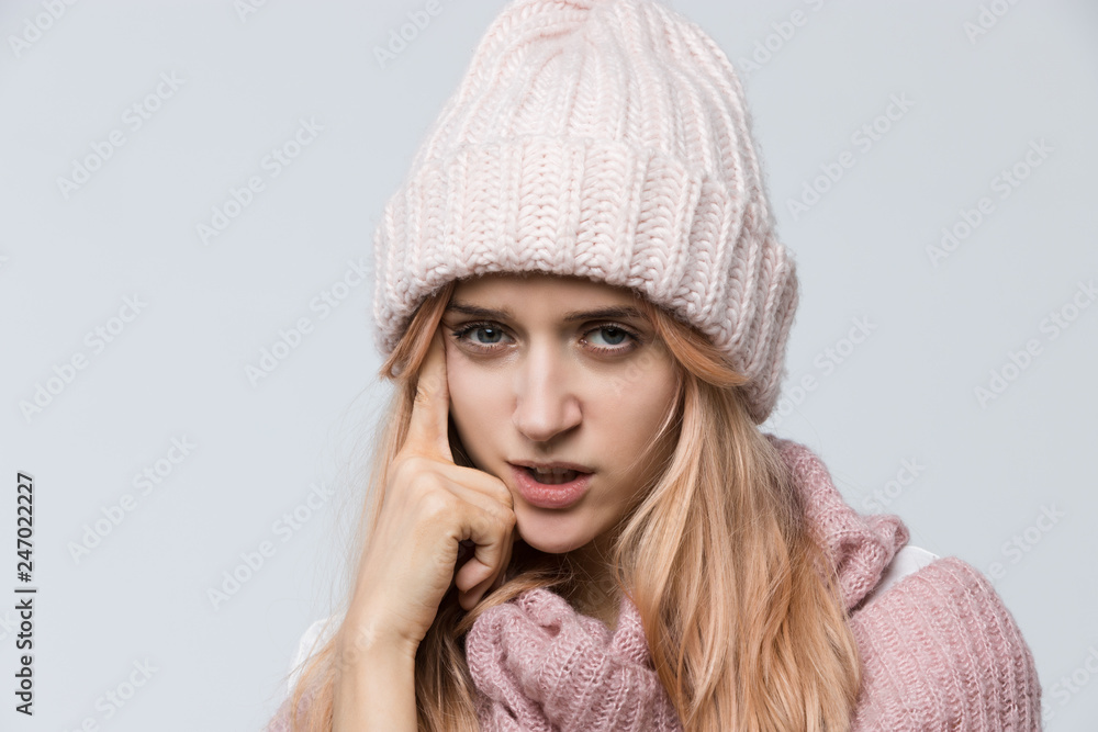 Cropped indoor portrait of pretty annoyed female in a pink sweater and white hat deep in thought/ doubts, irritated woman, trying to remember something important, people and emotions concept. Cropped indoor portrait of pretty annoyed female in a pink sweater and white hat deep in thought/ doubts, irritated woman, trying to remember something important, people and emotions concept.