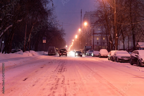 city road covered with snow with cars on the sidelines in winter season b