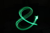 Long exposure, light painting photography.  Vibrant neon green ampersand symbol, grammar concept, against a black background