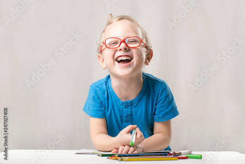 Happy child wears glasses, sits at the table and draws