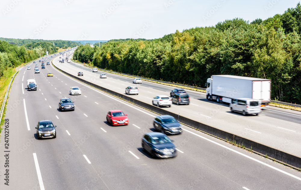 Heavy but fluid traffic on the eight-lane A10 highway in France in the  direction of Paris by a hot summer day with cars, vans, trailers and  semitrailer truck driving. Stock Photo