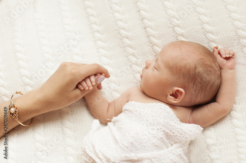 A young mom holds the hand of his newborn daughter. Hand in hand. Little baby hand in mom`s soft hands