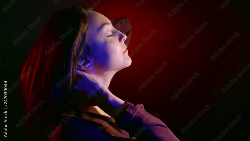 alluring young brunette girl is playing with her hair standing alone in dark room, red, blue and white lights alluring young brunette girl is playing with her hair standing alone in dark room, red, blue and white lights