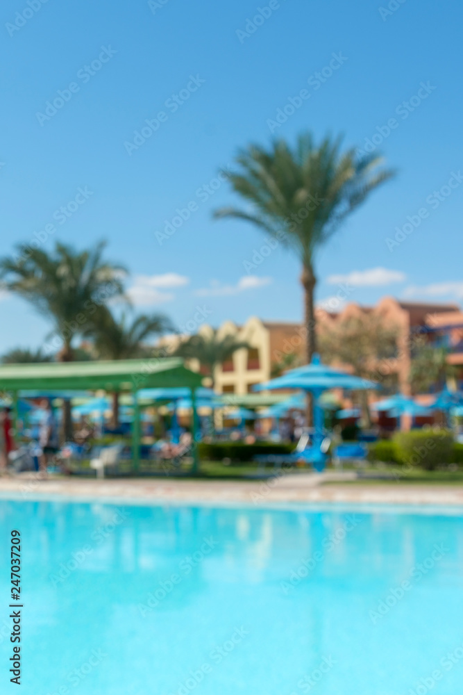 Blur summer background of pool with blue cool sky and tropical palm tree. vertical photo.
