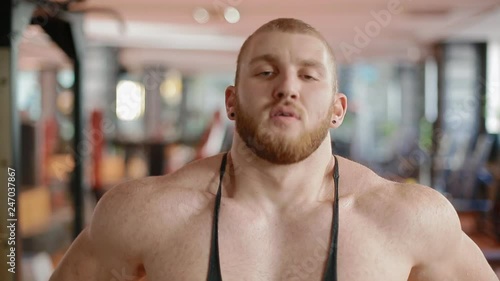 Close-up portrait of bearded white bodybuilder in the gym wearing sports jersey and breathing deeply. photo