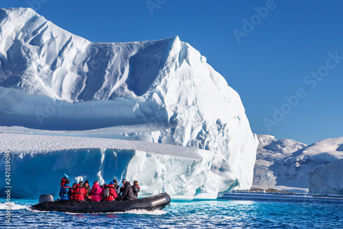 Tourists sitting on zodiac boat, exploring huge icebergs driftin