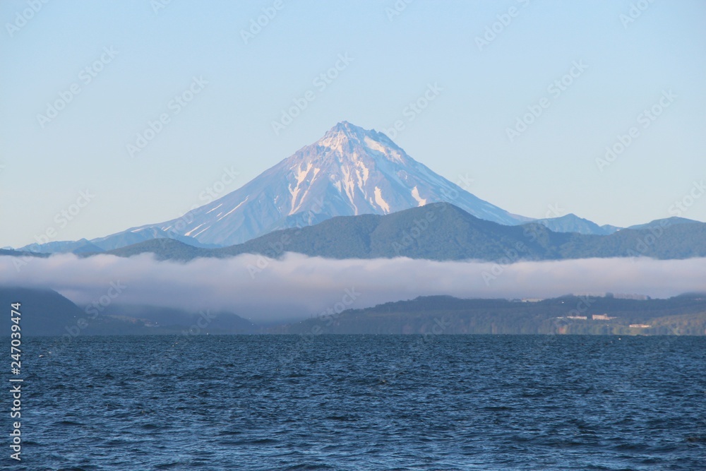 View of Vilyuchinsky volcano (also called Vilyuchik) from tourist boat. The cloud lies on the coastal cliffs. Vilyuchinsky is a stratovolcano in the southern part of Kamchatka Peninsula, Russia.
