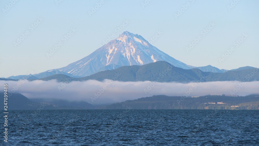 View of Vilyuchinsky volcano (also called Vilyuchik) from tourist boat. The cloud lies on the coastal cliffs. Vilyuchinsky is a stratovolcano in the southern part of Kamchatka Peninsula, Russia. View of Vilyuchinsky volcano (also called Vilyuchik) from tourist boat. The cloud lies on the coastal cliffs. Vilyuchinsky is a stratovolcano in the southern part of Kamchatka Peninsula, Russia.