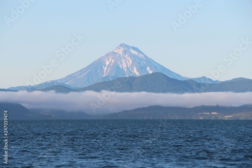 View of Vilyuchinsky volcano (also called Vilyuchik) from tourist boat. The cloud lies on the coastal cliffs. Vilyuchinsky is a stratovolcano in the southern part of Kamchatka Peninsula, Russia.