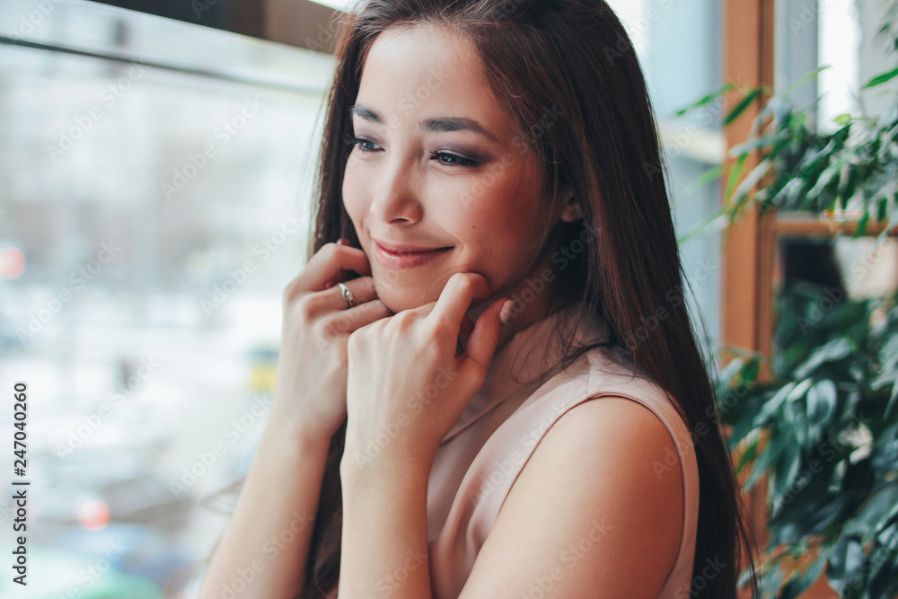 Portrait of beautiful charming romantic brunette smiling asian girl near the window at cafe