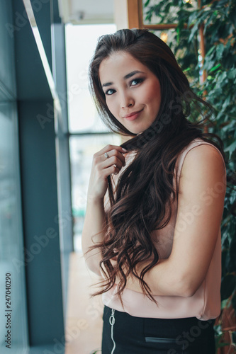 Portrait of beautiful charming romantic brunette smiling asian girl with long hair near the window at cafe