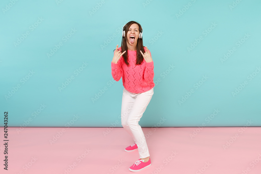 Full length portrait of happy young woman in knitted rose sweater, white pants, headphones isolated on bright pink blue pastel wall background in studio. Fashion lifestyle concept. Mock up copy space. Full length portrait of happy young woman in knitted rose sweater, white pants, headphones isolated on bright pink blue pastel wall background in studio. Fashion lifestyle concept. Mock up copy space.