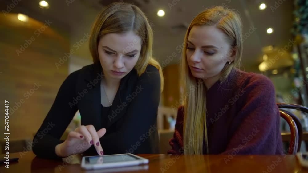 two serious female students are writing message by tablet, one is typing, second is looking at screen two serious female students are writing message by tablet, one is typing, second is looking at screen