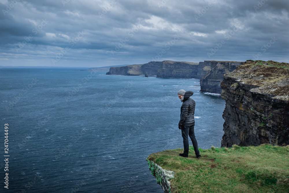 Man standing at a cliff by the Cliffs of Moher