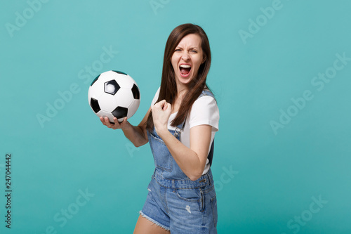 Screaming wild young woman football fan cheer up support favorite team with soccer ball doing winner gesture isolated on blue turquoise wall background. People emotions, sport family leisure concept. © ViDi Studio