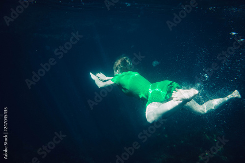 short-haired girl in a green dress swims underwater in the sea