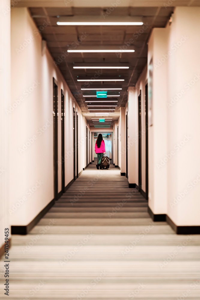 Silhouette of an unrecognizable girl in away of corridor with her luggage, arrival at the hotel