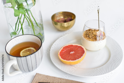 Healthy breakfast. Ingredients: grapefruit, granola, tea, lychee. Vase of roses. Side view, white background.