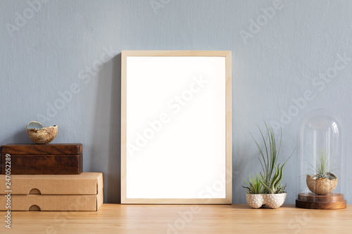 Modern home interior with mock up photo frame on the brown wooden table with office accessories, boxes, beautiful air plant in stylish pot. Grey walls. Minimal decor of home office desk.