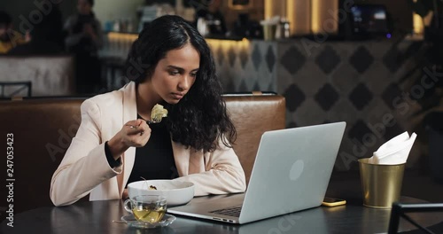 Business woman sitting with a laptop in the cafe and eating dinner with a cup of tea on the table. Eating lunch at work desk