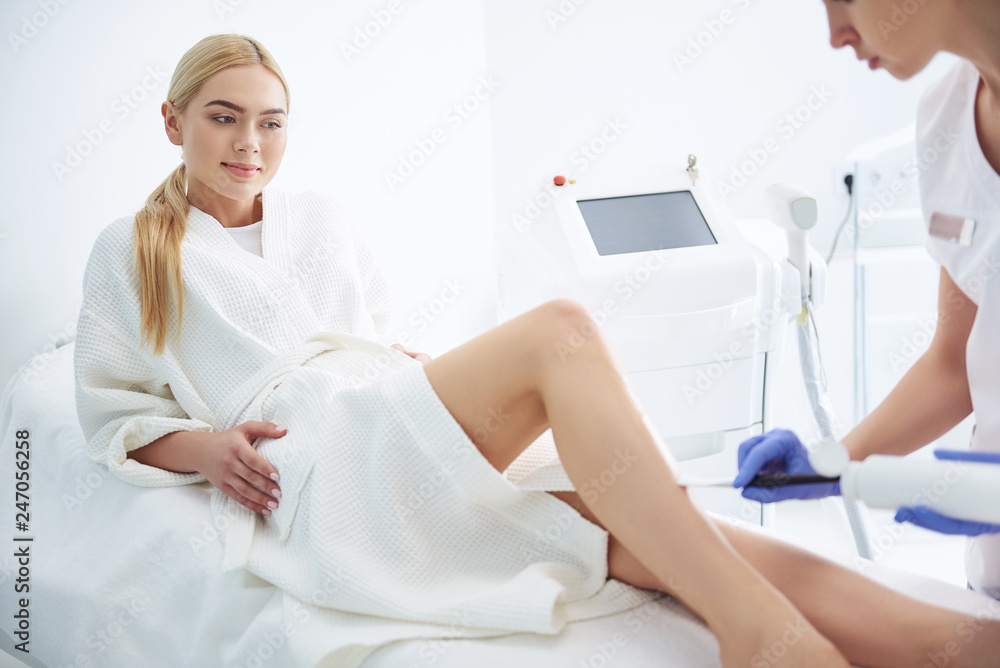 Young lady watching how beautician applying gel on her leg Young lady watching how beautician applying gel on her leg