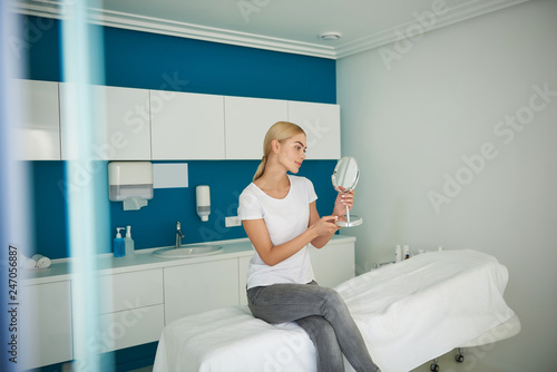 Slika na platnu Beautiful young lady sitting on daybed and holding looking-glass
