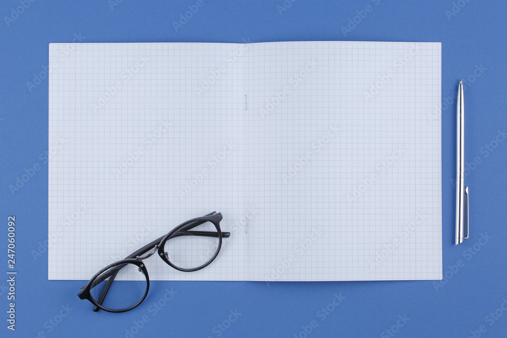 Fototapeta premium school notebook with pen and glasses on a blue table