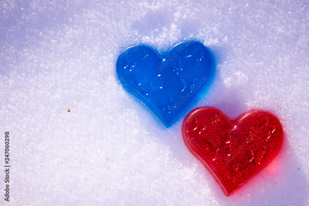 Fototapeta premium Two hearts are red and blue in the snow. Handmade soap in the shape of a heart. Love and valentines day concept. Romantic background with free space for text.