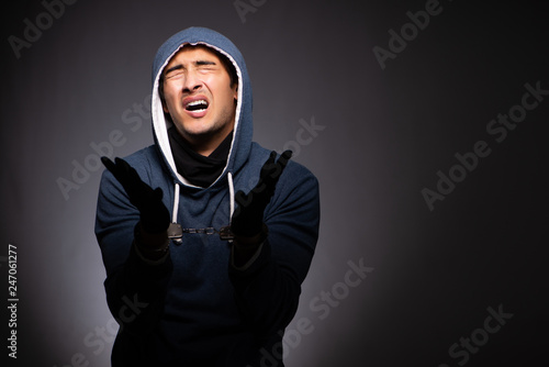 Young gangster in hood on grey background 
