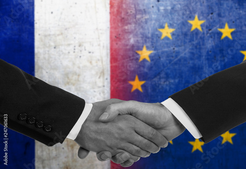 Two men/politicians in suits shaking hands with the national flags on the background - European Union and France