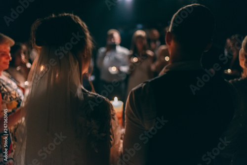 Bride, groom holds wedding candles in his hands. Burning candle Spiritual couple holding candles during a wedding ceremony in a christian church, view from the back. Defocus
