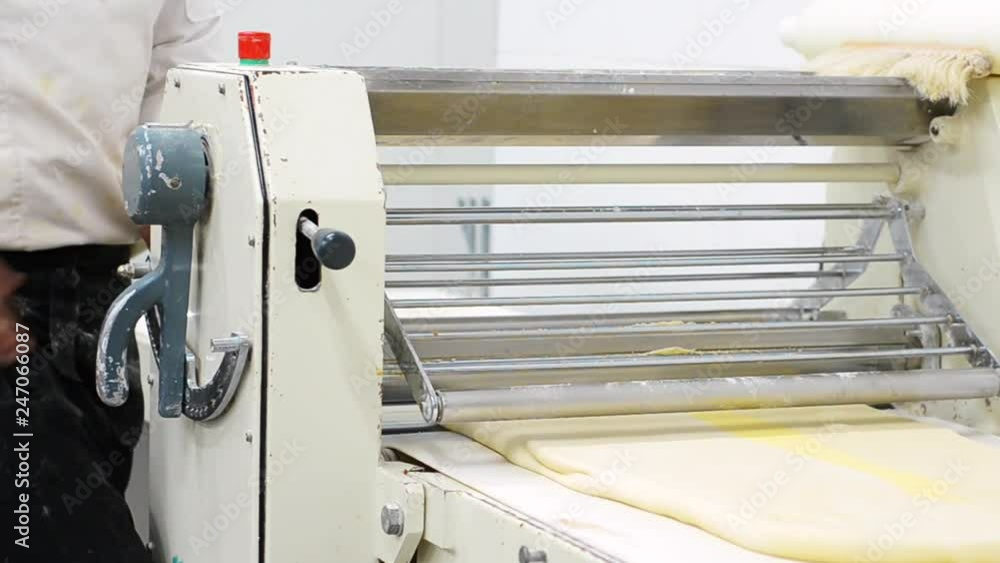 Baker using dough sheeter machine to produce croissants dough at the bakery . Baker using dough sheeter machine to produce croissants dough at the bakery .