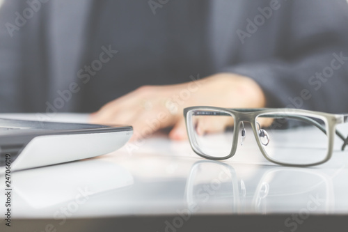Eine Frau arbeitet und hat eine Brille neben einem Laptop auf den Schreibtisch gelegt. 