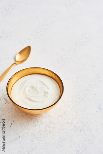 Bowl of fresh Greek yoghurt and golden spoon on white abstract background. Healthy breakfast. Golden utensils. Top view. Copy space for text.