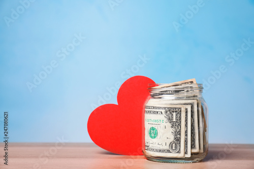 Red heart and donation jar with money on table against color background. Space for text