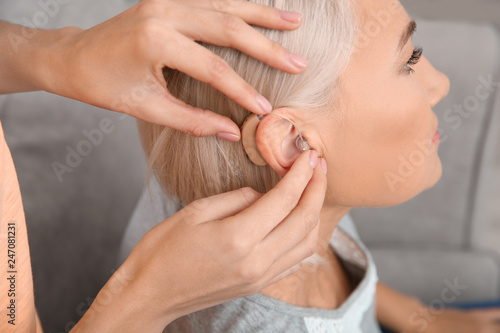 Young woman putting hearing aid in mother's ear indoors, closeup