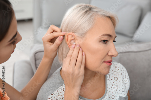 Foto Young woman putting hearing aid in mother's ear indoors