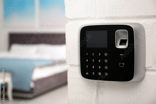 Modern alarm system with fingerprint scanner on brick wall in house. Space for text