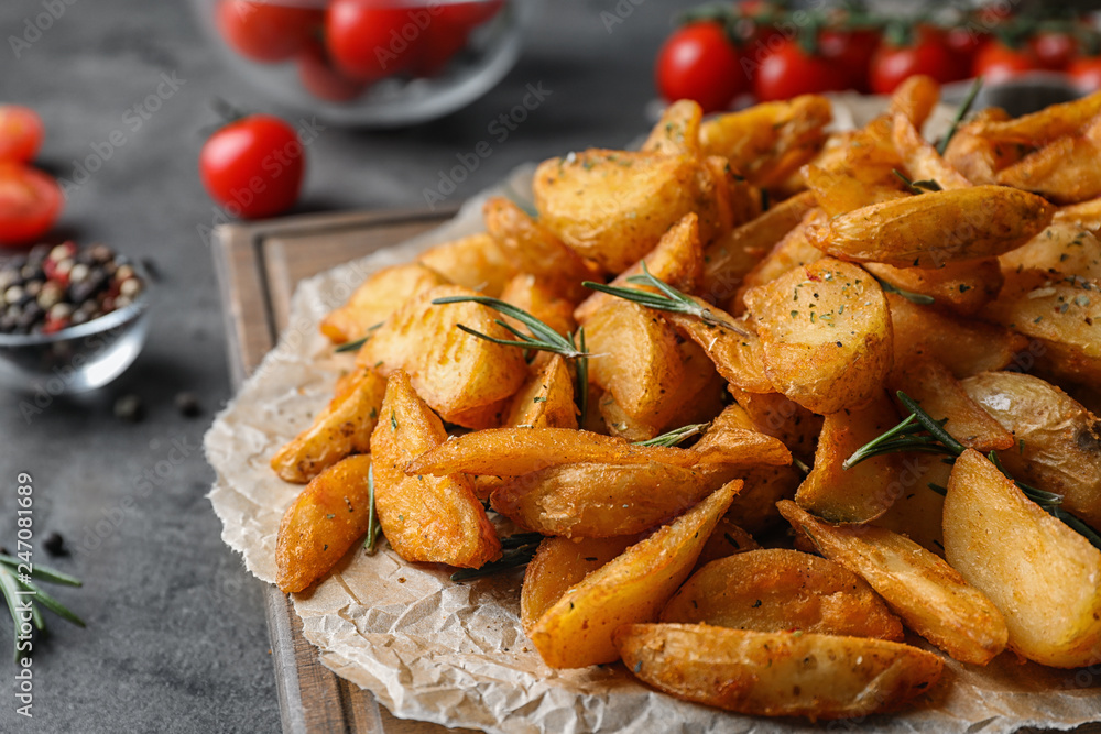 Wooden board with baked potatoes and rosemary on table, closeup Wooden board with baked potatoes and rosemary on table, closeup