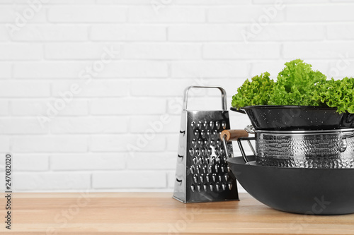 Set of clean cookware and lettuce on table against  white brick wall. Space for text