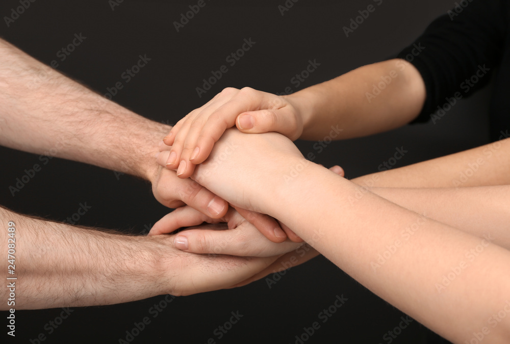 Young people putting their hands together on dark background, closeup