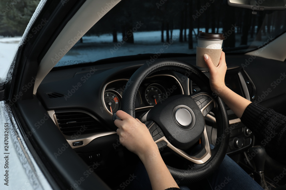 Young woman with coffee driving car along winter forest, closeup