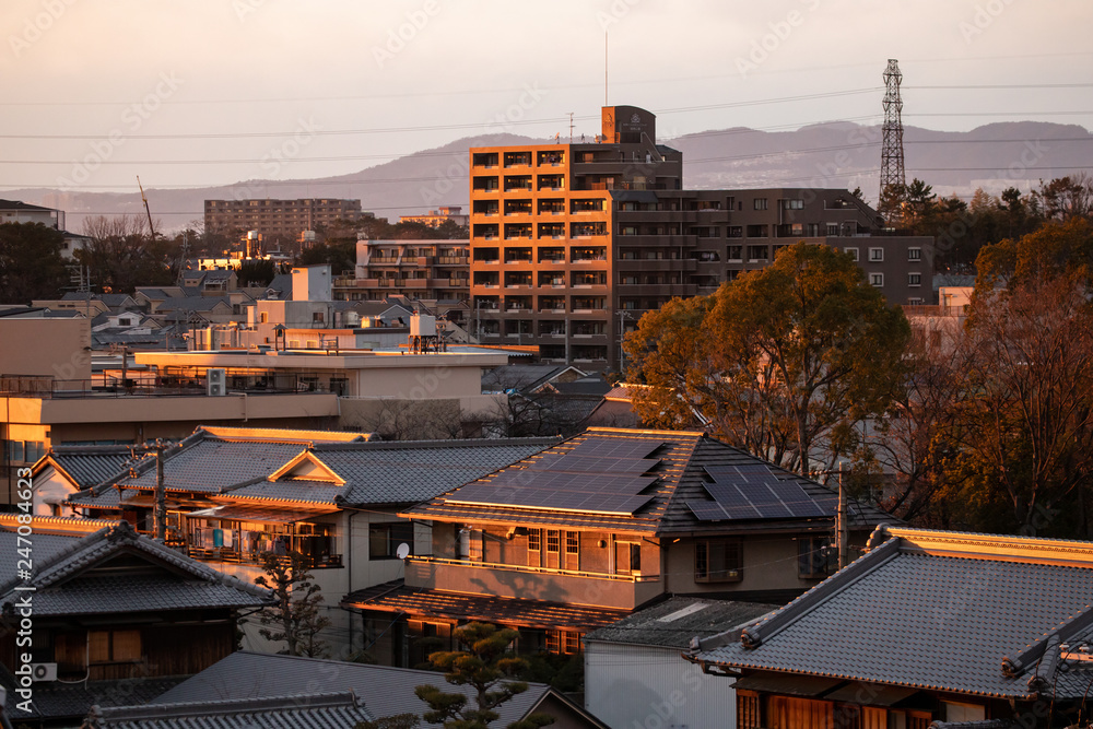 Solar panels on roof of traditional Japanese house in city at sunset