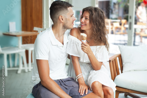 portrait of a smiling young couple in white with ice cream cone. Man and woman looking to each other. Cafe, interior