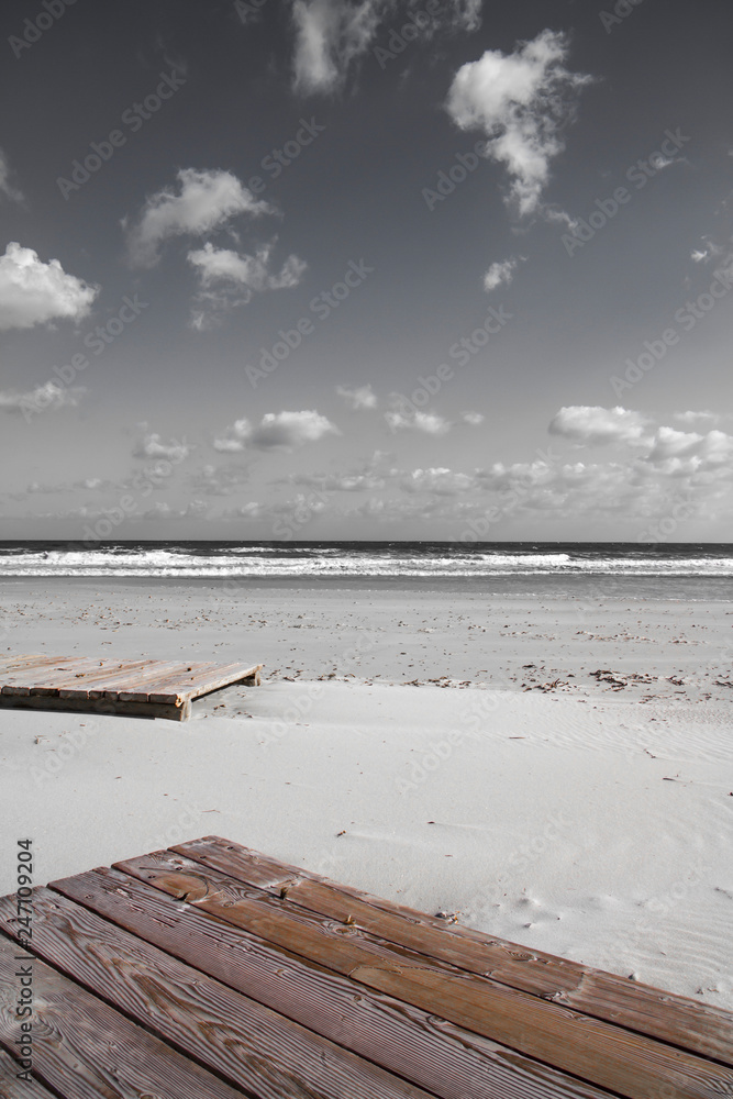 Boardwalk in the winter sea. In the solitude of the finished season the wooden platforms lie abandoned on the white sand, moved by the impetuous sea
