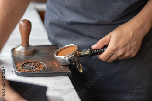 Barista using a tamper to press ground coffee into a portafilter. Close up photo